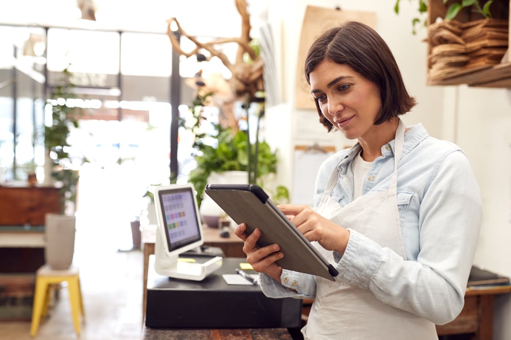 Mujer en un comercio minorista interactuando con una tablet, revisando su planificación estratégica de negocios.